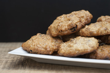 Homemade oatmeal cookies in white square plate,on wooden board and Black background. Sweet dessert snack, Healthy Food. Copy space.