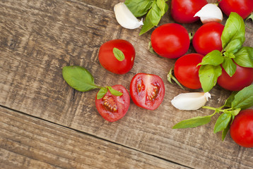 Fresh cherry tomatoes on rustic wooden board. Basil leaves and garlic in the background. Healthy food ingredients.