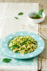 Pasta with pesto sauce, green peas and basil on a wooden table. Rustic style.