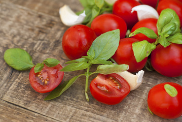 Fresh cherry tomatoes on rustic wooden board. Basil leaves and garlic in the background. Healthy food ingredients.