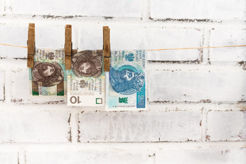 Three Polish zloty bills attached with old wooden washing clips hanging on the string on the white shabby bricks background