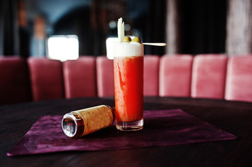 Alcoholic long cocktail with olives in glass at bar table.