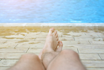 Hairy legs of a man against a background of pure blue water in a pool. A tired man finally relaxed by the water. The concept of the long-awaited holiday. All inclusive.
