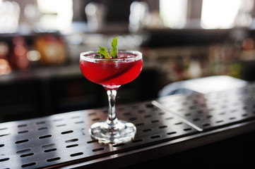 Alcoholic red cocktail with mint on bar table.