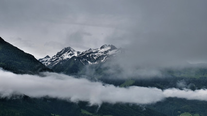 Hochgebirge in Österreich, im Vordergrund steigt Nebel aus dem Tal hoch, im Hintergrund Berge mit Schnee