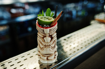 Alcoholic cocktail with mint and lime in originally voodoo earthen glass on bar table.