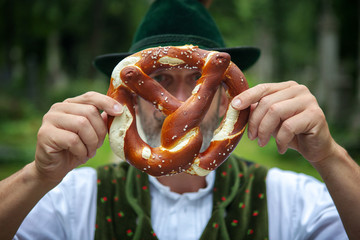 bavarian man holding a pretzel in front of his face - obrazy, fototapety, plakaty