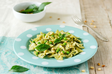 Pasta with pesto sauce, green peas and basil on a wooden table. Rustic style.