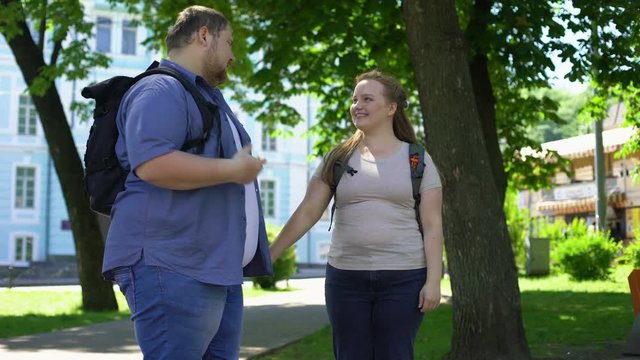 Young overweight man and woman holding hands and nuzzling in park, students love