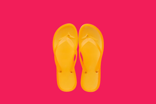Yellow beach flip flops on neon pink background