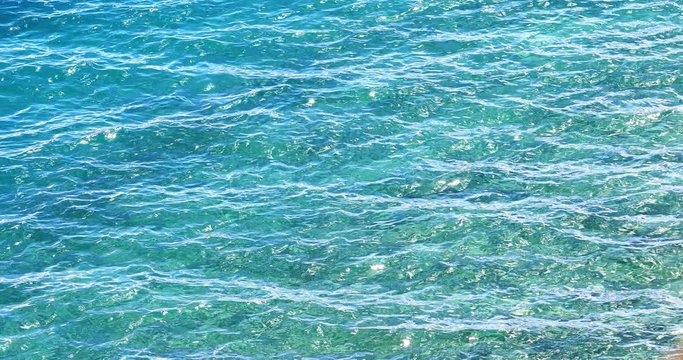 Crystal clear and transparent water surface texture of turquoise sea waves in tropics. Shiny ripples reflect sunlight at sunny day. Tranquil and serene meditative background