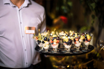 The waiter holds a tray with desserts.