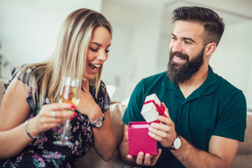 Smiling young man surprising cheerful woman with a gift box at home