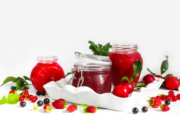 assortment of jams, seasonal fresh berries and fruits on white background