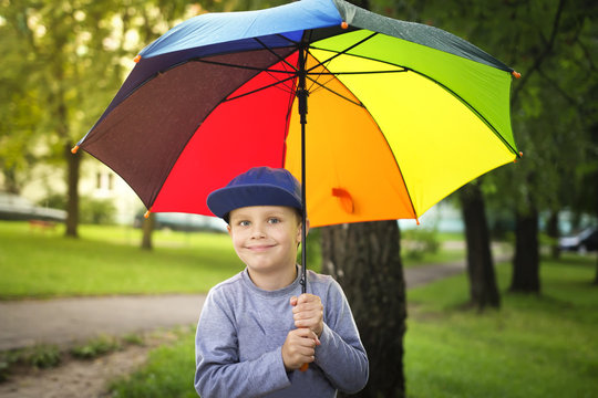 Little caucasian boy with colorful umbrella in park after rain on sunny summer day
