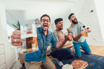 Happy male friends watching sports on tv and drinking beer.
