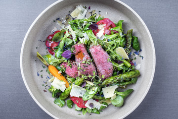 Modern style spring salad with barbecue dry aged sliced fillet steak and green asparagus as top view on a plate