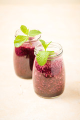 Fresh raw blended drink with blueberries and green mint leaves on pastel yellow background.