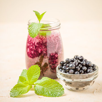 Blueberry fresh smoothie with ripe wild forest berries and green mint leaves on pastel yellow background.