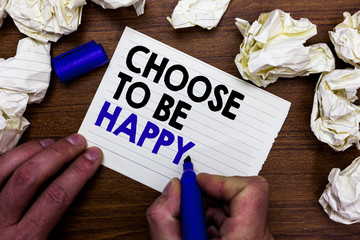 Writing note showing Choose To Be Happy. Business photo showcasing Decide being in a good mood smiley cheerful glad enjoy Hand holding marker write words paper lob scatter around woody desk.