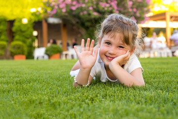 Adorable smiling girl laying in the grass and waved her hand 
