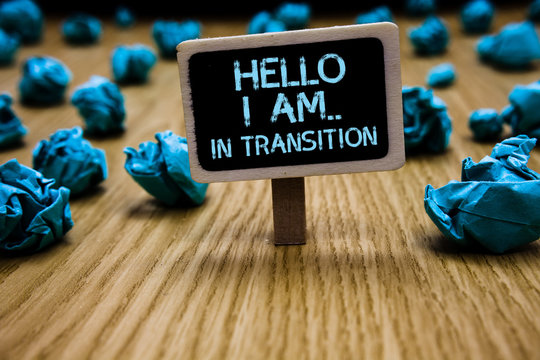 Word writing text Hello I Am.. In Transition. Business concept for Changing process Progressing planning new things Paperclip hold black paperboard with text blue paper lobs on wooden floor.