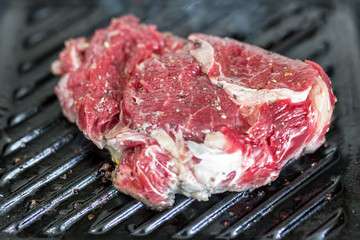 Close-up raw tasty fresh rib eye steak on grill cast iron pan. Organic beef meat seasoned with ground pepper coocked on barbeque