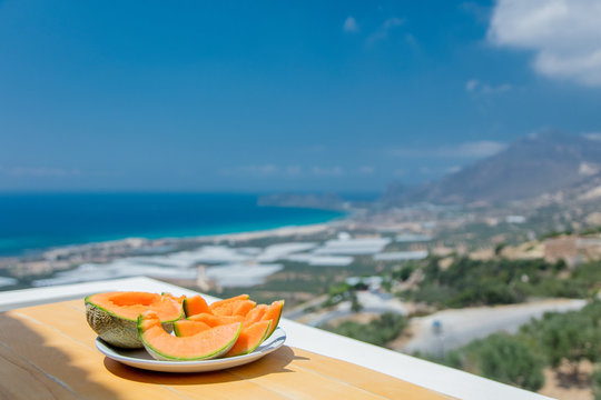 Yellow melon on a plate on a table with view on sea and mountain. Falassarna, Crete, Greece