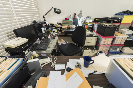 Messy business office with piles of files and disorganized clutter.