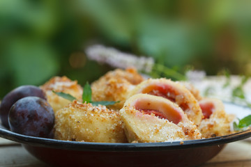 Closeup of a plate with delicious sweet plum dumplings. Outdoor image with green blurred background.
