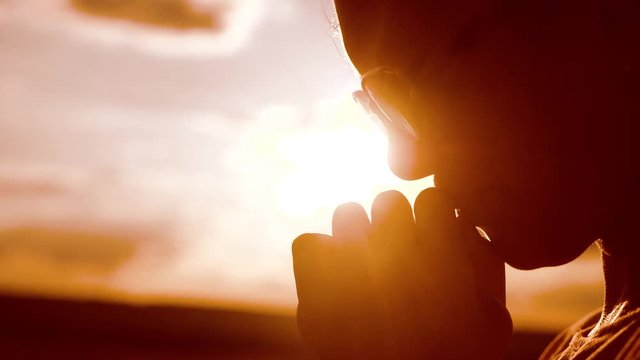 the girl prays. Girl folded her hands in prayer silhouette at sunset. slow motion video. Girl folded her hands in prayer pray to lifestyle God. girl praying asks forgiveness for sins of repentance