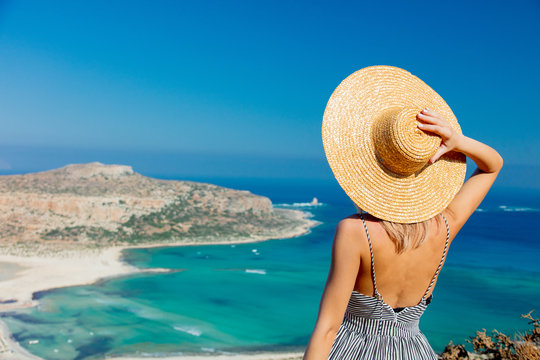 Young redhead girl in hat and dress with sea coastline on Balos, Crete, Greece