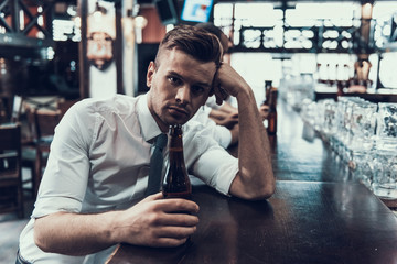 Sad Young Man with Bottle of Beer Sitting in Bar.