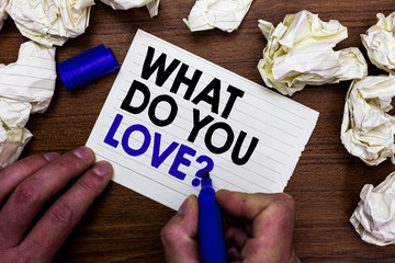 Writing note showing What Do You Love question. Business photo showcasing Enjoyable things passion for something inspiration Hand holding marker write words paper lob scatter around woody desk.