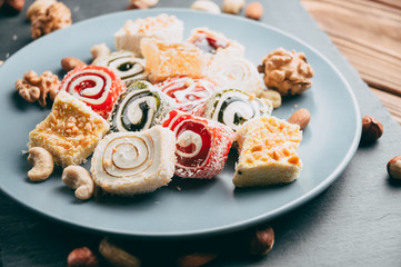 Traditional oriental sweets and nuts: hazelnuts, cashews on a brown wooden background. Turkish dessert is the locus of Rahat. View from above. Place under the text.