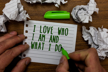 Word writing text I Love Who I Am And What I Do. Business concept for High self-stem being comfortable with your job Hand hold green pen and words on white page paper lobs around on wooden desk.