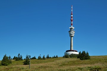 Fototapeta premium Red and white telecommunication and lookout tower Praded, Czech Republic, Europe standing on a hill in Jeseniky mountains, sunny summer day, clear blue sky, green trees 