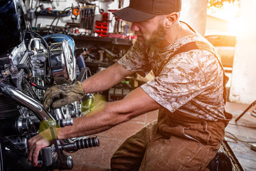 Side view portrait of man working in garage repairing motorcycle and customizing it