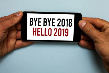 Word writing text Bye Bye 2018 Hello 2019. Business concept for Starting new year Motivational message 2018 is over Human hand hold smartphone with red and black letters on shadow blue floor. © A