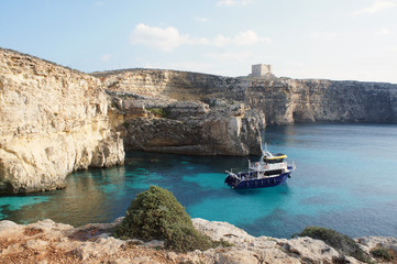 Boat on the lagoon with high cliffs and Santa Marija Tower on Commino Island in Malta (Torri ta' Kemmuna)