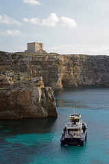 Boat on the lagoon with high cliffs and Santa Marija Tower on Comino Island in Malta (Torri ta' Kemmuna)