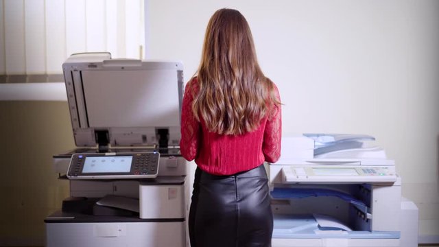 Girl printing in the office. Young beautiful woman making copies of files in the copy machine. Assistant manager working at the office.