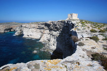 Blue lagoon with high cliffs and Santa Marija Tower on Commino Island in Malta (Torri ta' Kemmuna)