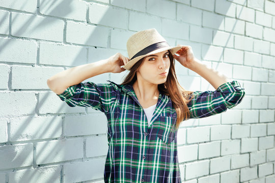 Happy young woman in hat and plaid shirt make faces, near blue brick wall