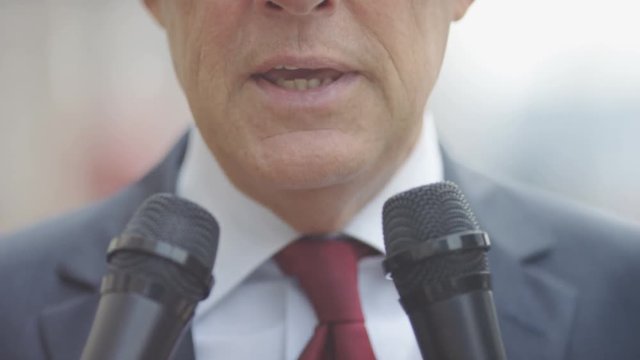 Close up mouth of of mature male addressing questions to microphones