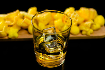 glass of whiskey with ice cubes and salty snacks on the background of the bar