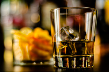 glass of whiskey with ice cubes and salty snacks on the background of the bar
