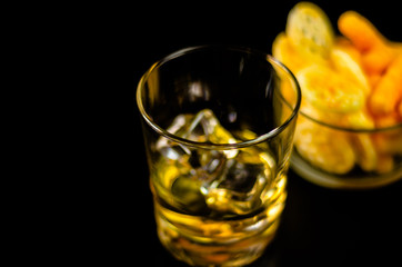 glass of whiskey with ice cubes and salty snacks on the background of the bar