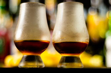 glass of whiskey with ice cubes and salty snacks on the background of the bar