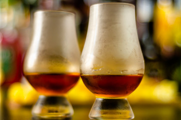 glass of whiskey with ice cubes and salty snacks on the background of the bar